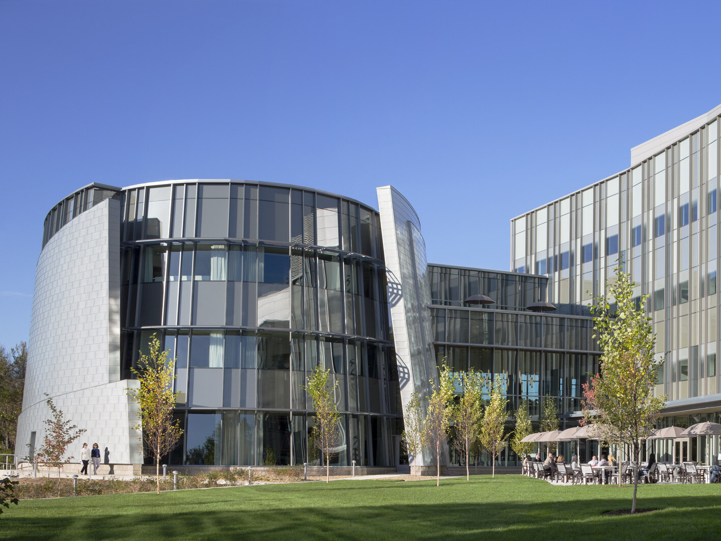 exterior of a world renowend genomic medical center in Connecticut; round glass from anchors one end of the building with an outdoor patio beneath facade with glass fenestration