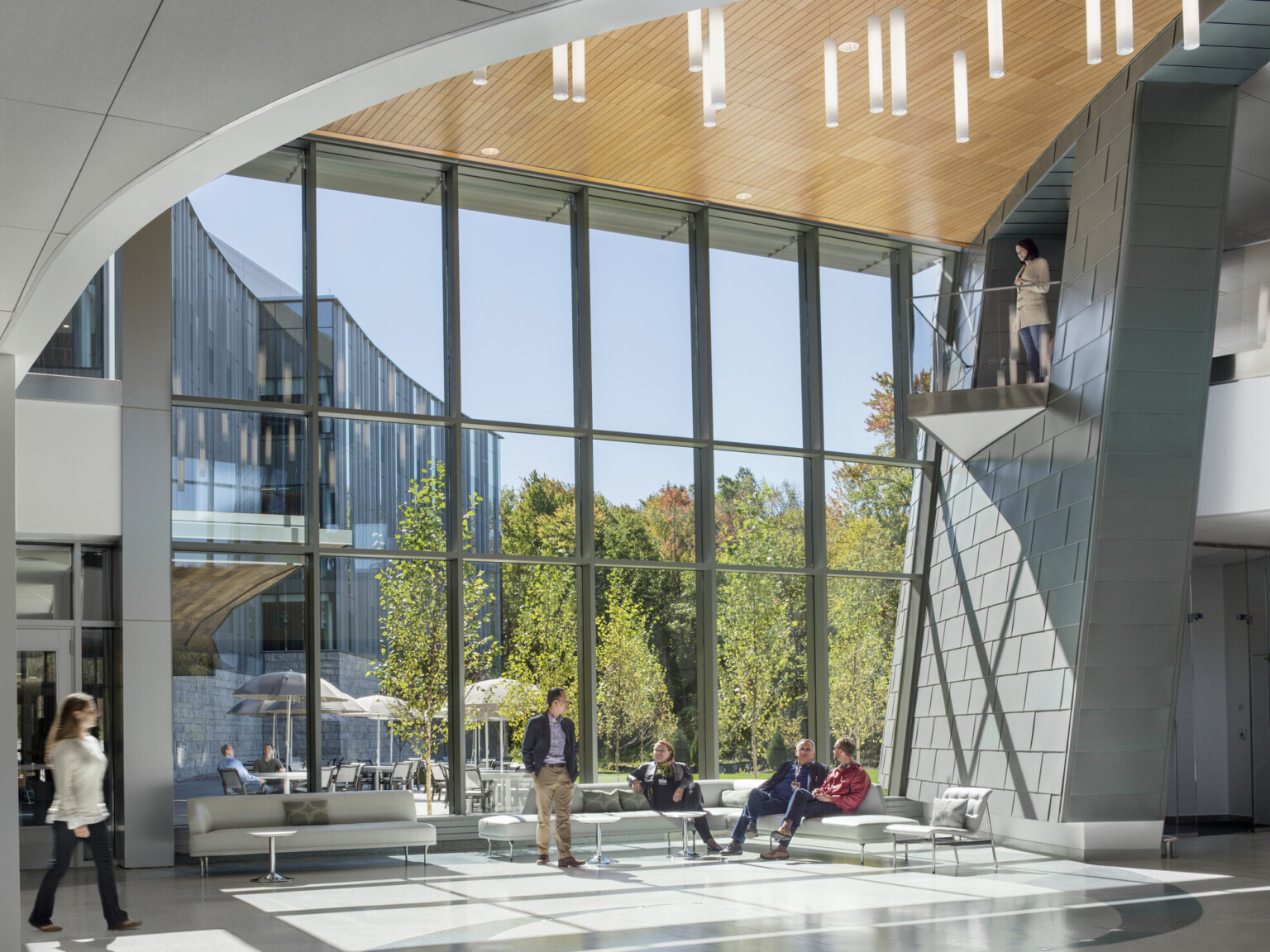 main level lobby area of medical learning center, large atrium with double height windows bring in natural light, curved upper floor has balcony overlooking the space, wood ceiling