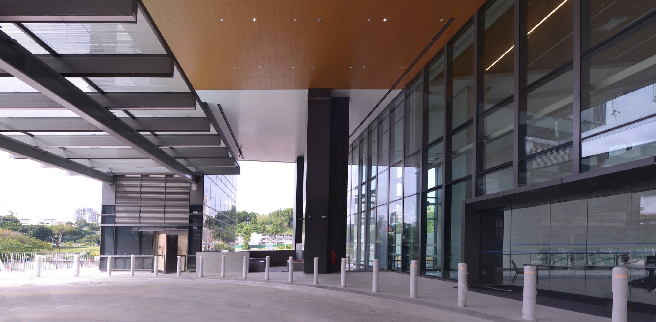 Exterior of a modern medical building with large glass windows and a spacious covered entrance area. The ceiling of the entrance area is lined with recessed lights, and there are several vertical pillars along the edge of the walkway.