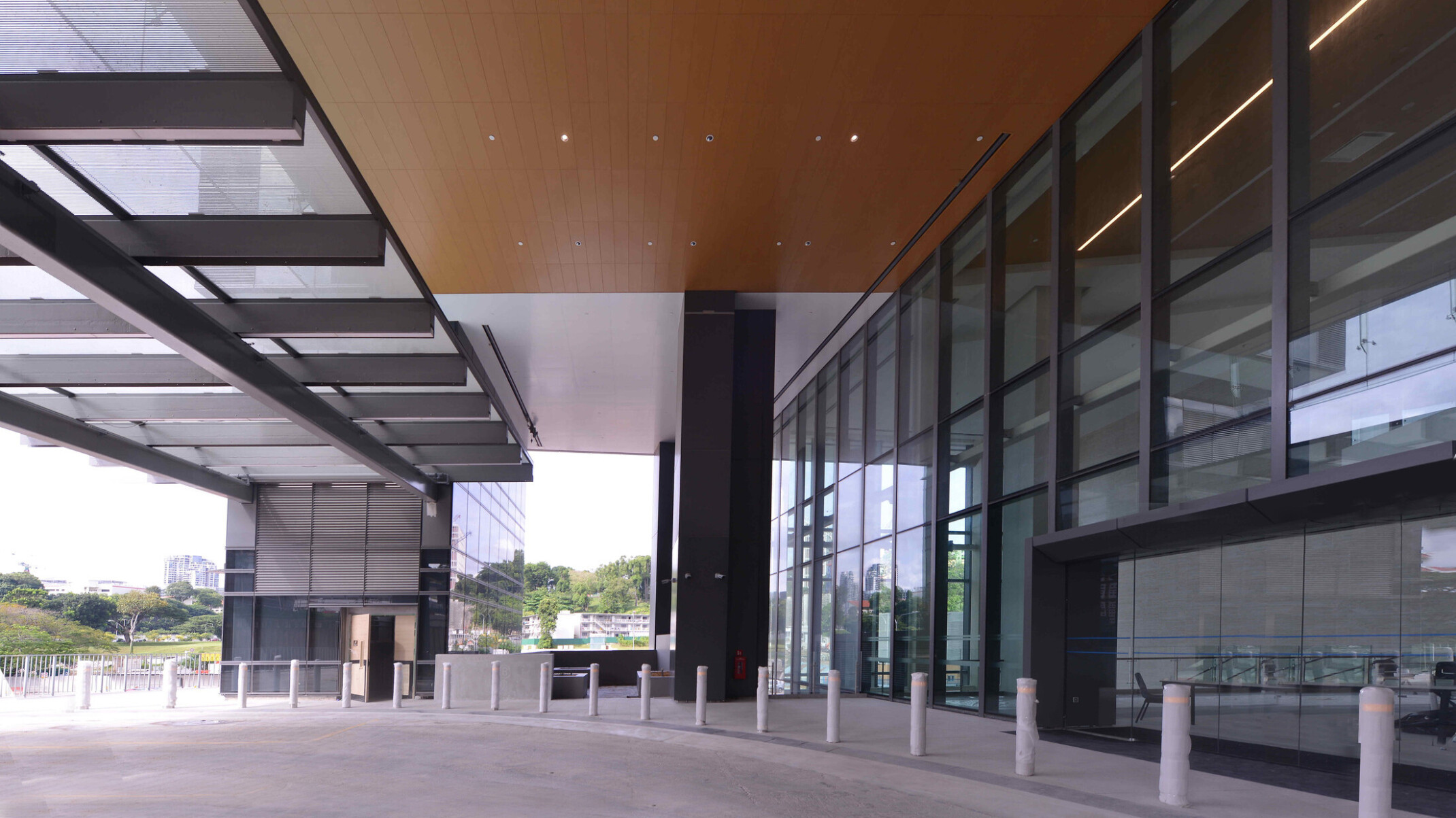 Exterior of a modern medical building with large glass windows and a spacious covered entrance area. The ceiling of the entrance area is lined with recessed lights, and there are several vertical pillars along the edge of the walkway.
