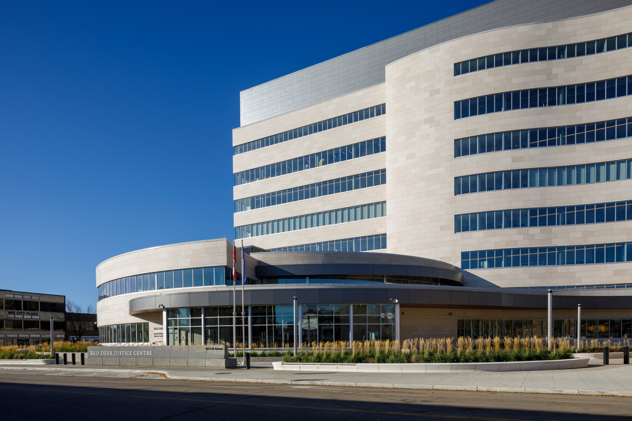 Daytime street view of the Red Deer Justice Centre’s curved, multi-story facade with integrated landscape beds of native plants.
