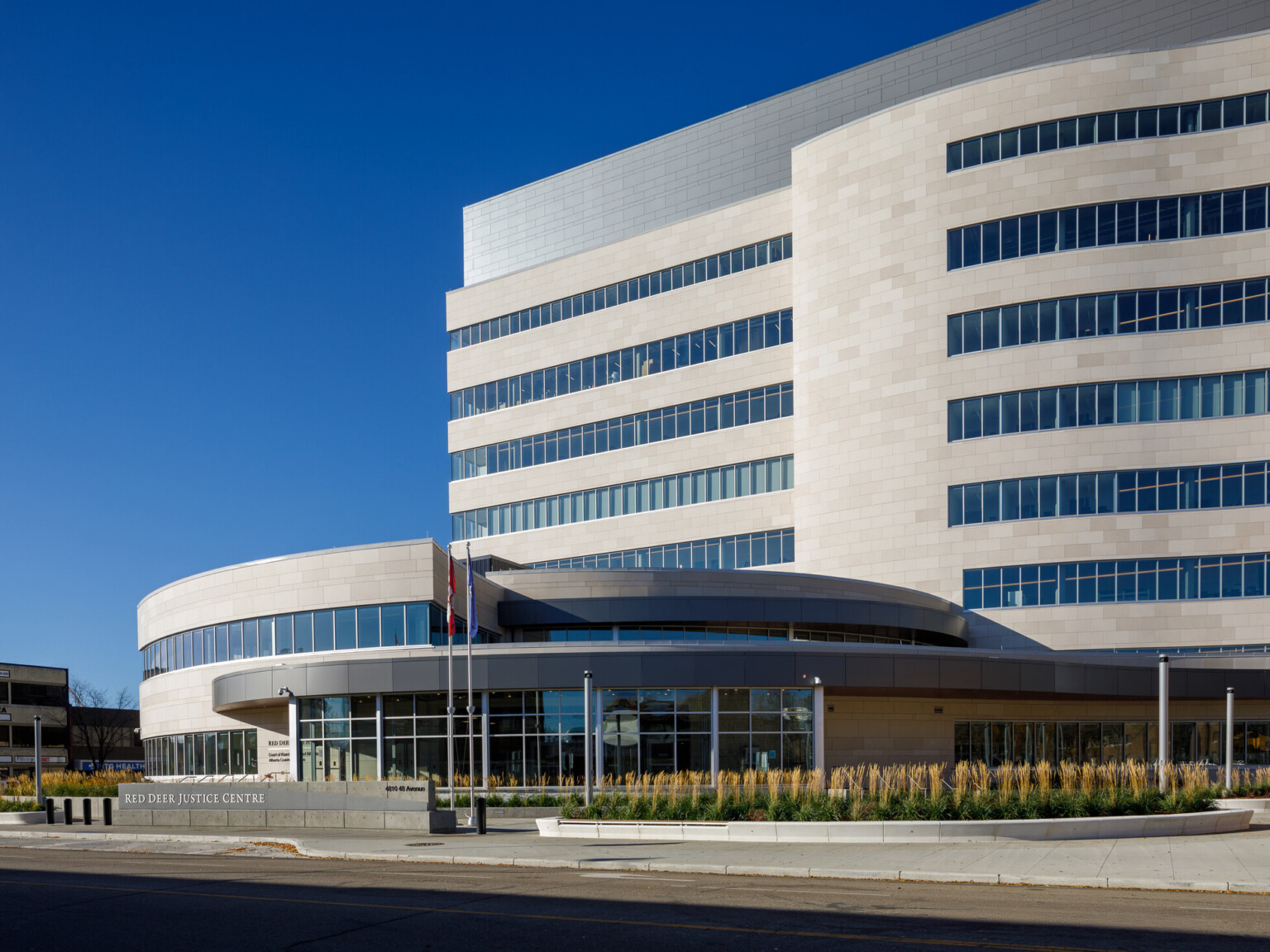 Daytime street view of the Red Deer Justice Centre’s curved, multi-story facade with integrated landscape beds of native plants.