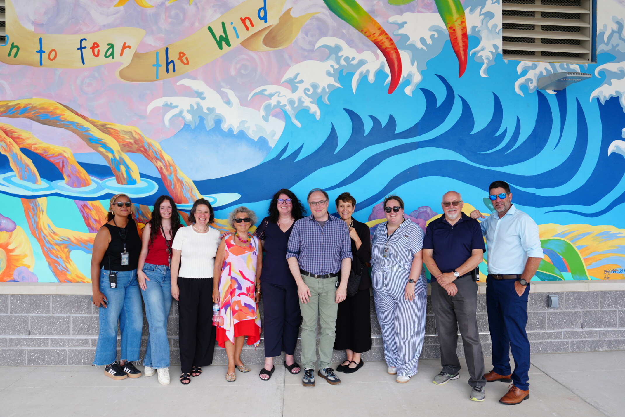 Team of people standing in front of a large art mural of the ocean
