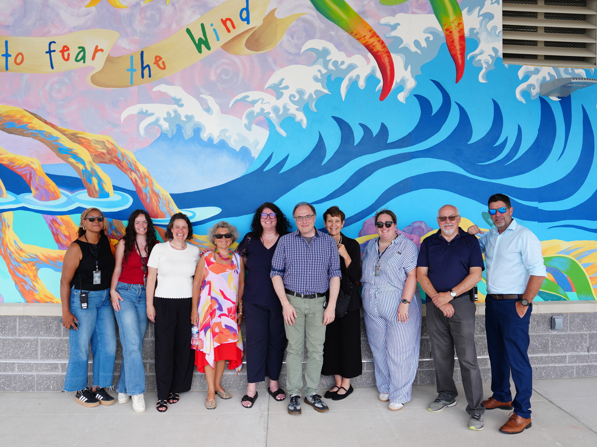 Team of people standing in front of a large art mural of the ocean