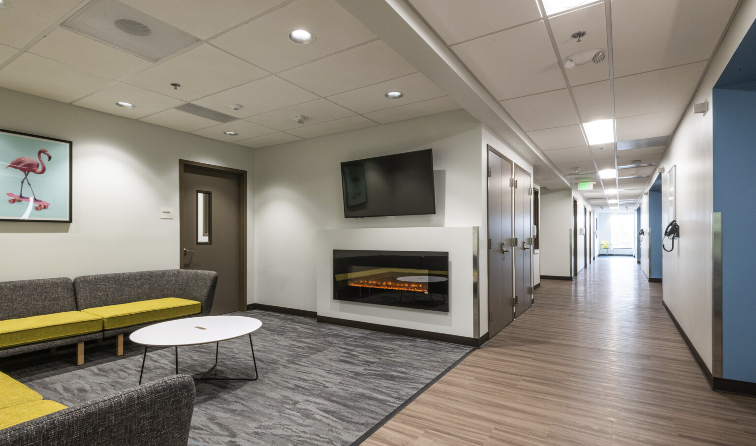 A gray sectional sofa with chartreuse seat cushions in front of a fireplace and TV next to hallway with doors and wood floors