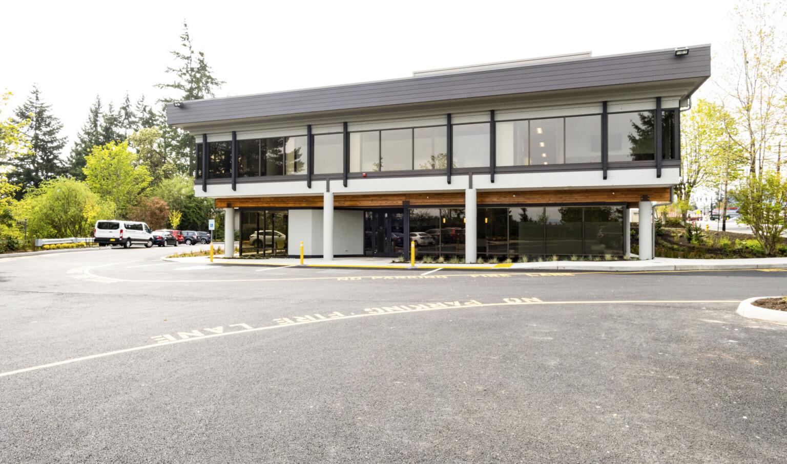 modern building with wooden fascia and white pillars on the first floor, floor to ceiling glass and black fascia on floor 2