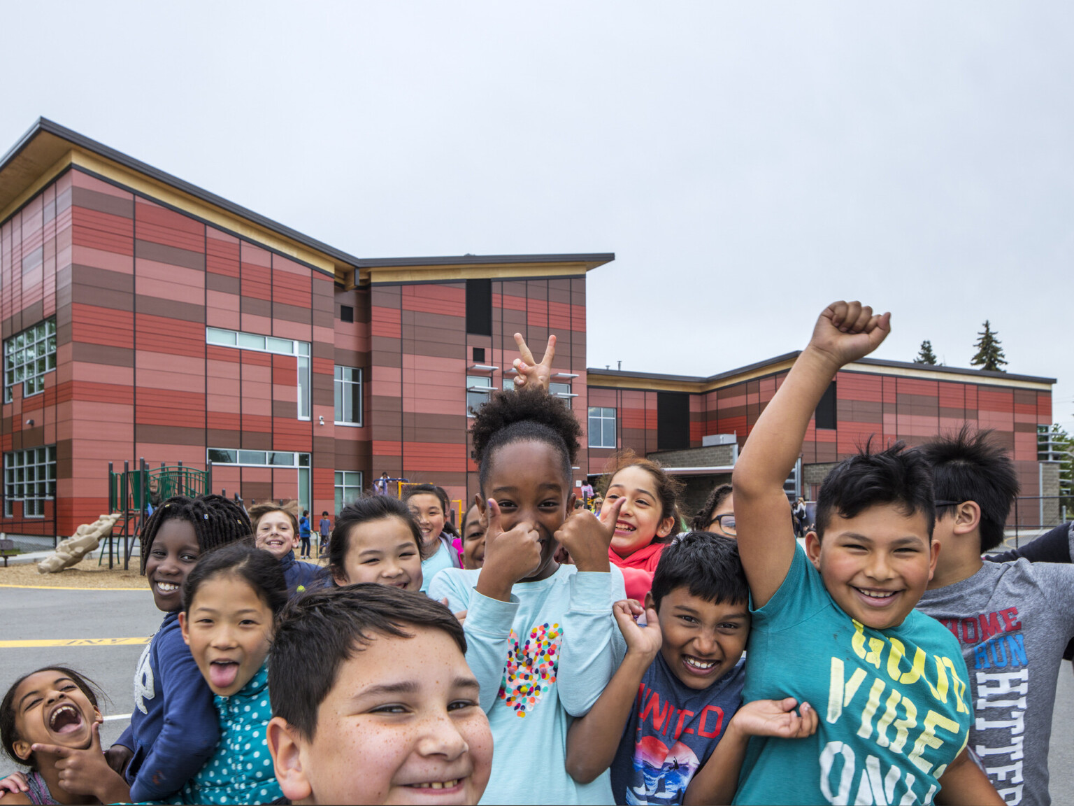 group of students gather in front of camera outside Lake Stickney Elementary School, a red paneled building with angled roof