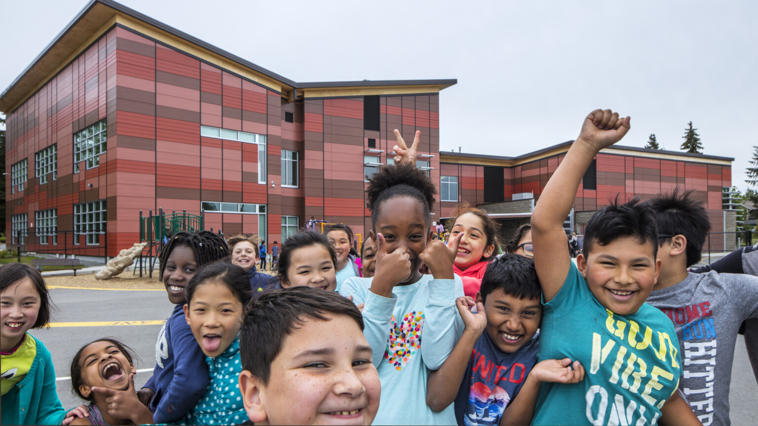 group of students gather in front of camera outside Lake Stickney Elementary School, a red paneled building with angled roof