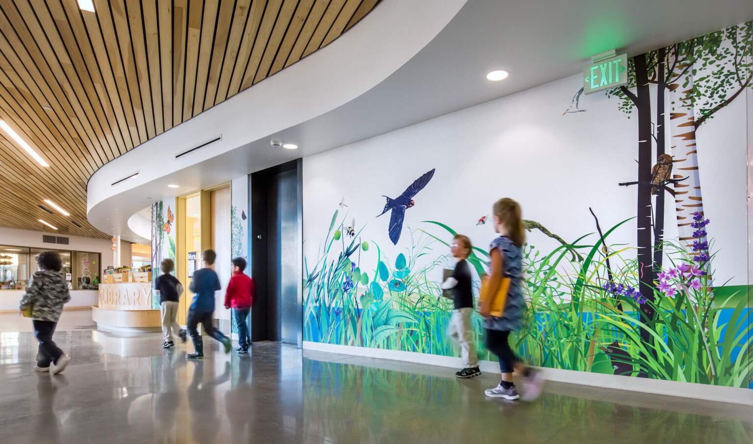 A curved hallway with wood panel ceiling and a mural along the wall of grass and animals. Wood desk curves with hall