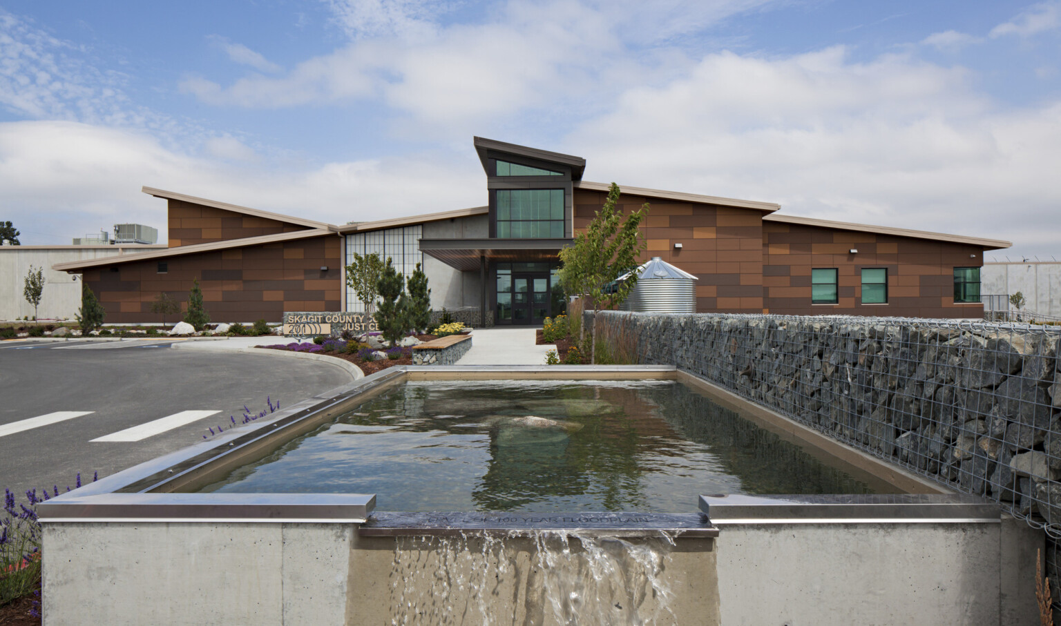 The Skagit County Community Justice Center, a stone building with central entryway. Front is water feature and stone gabion