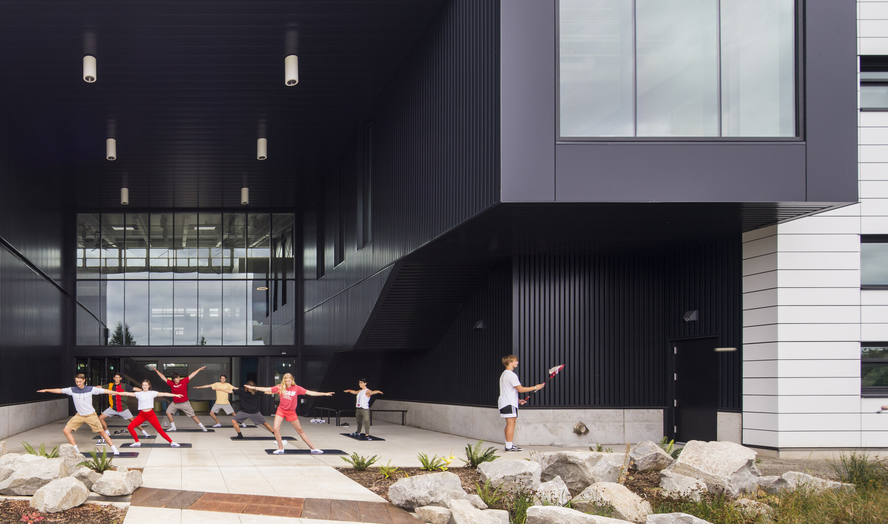Exterior view, atrium is recess and patio is covered. Right, the building extends in a black tunnel with large window at end
