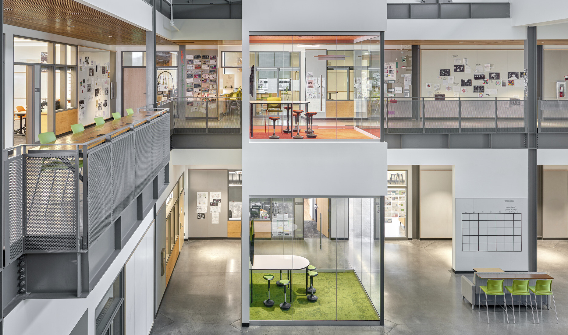 Viewed of atrium from the top of the stairs facing learning pods. 2nd floor hallway has wall collages and high top table