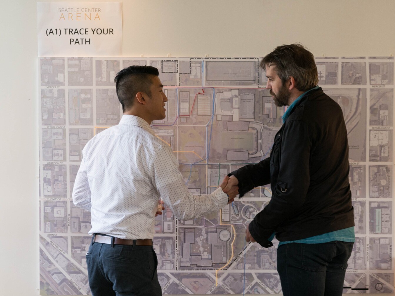 Two men shaking hands in front of a large map on a wall.