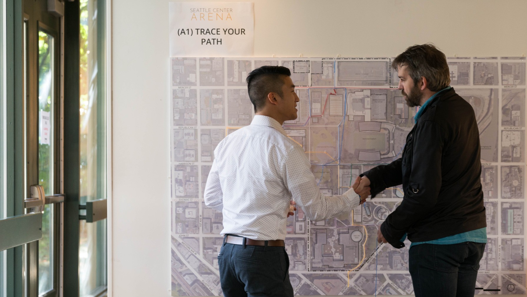 Two men shaking hands in front of a large map on a wall.