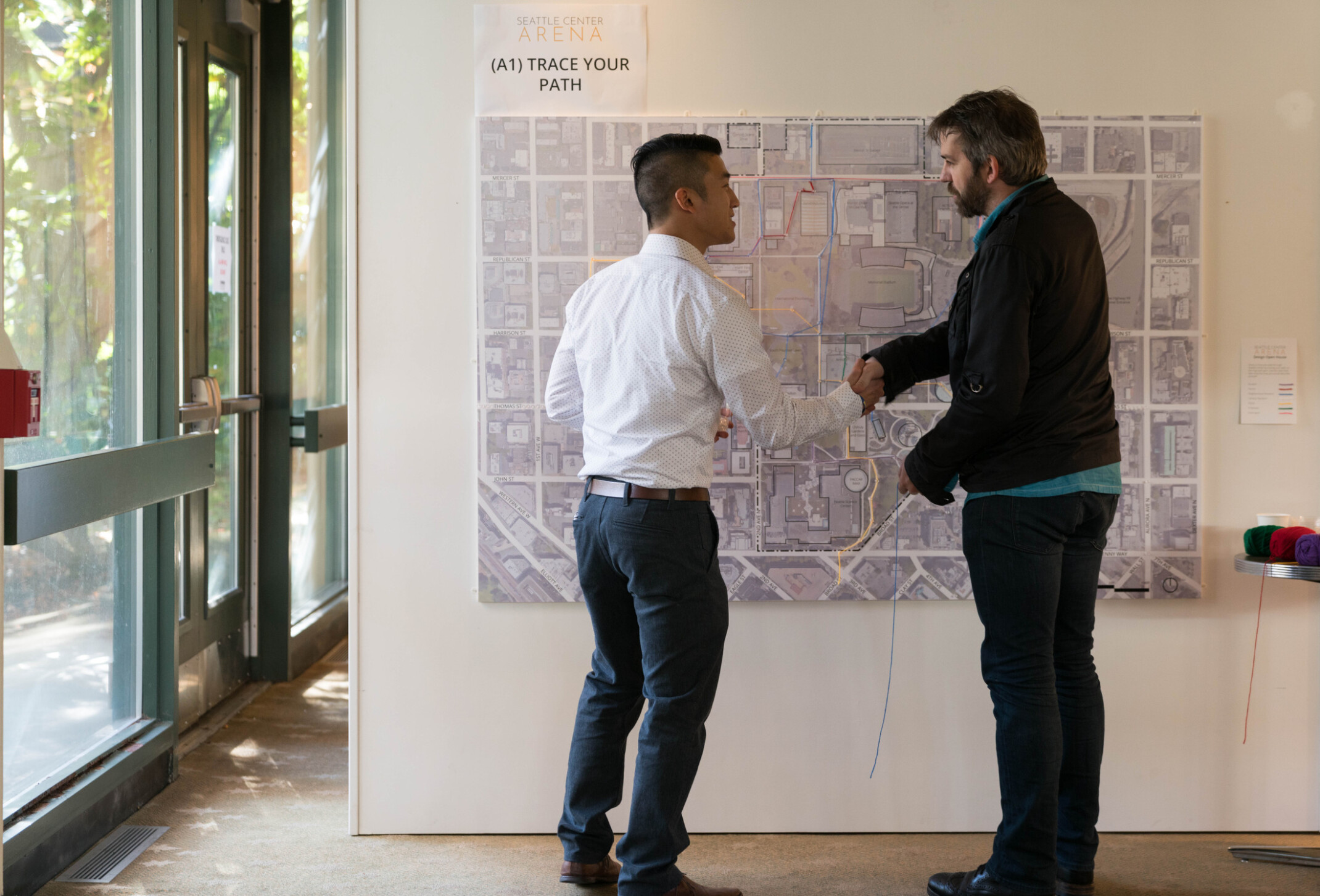 Two men shaking hands in front of a large map on a wall.