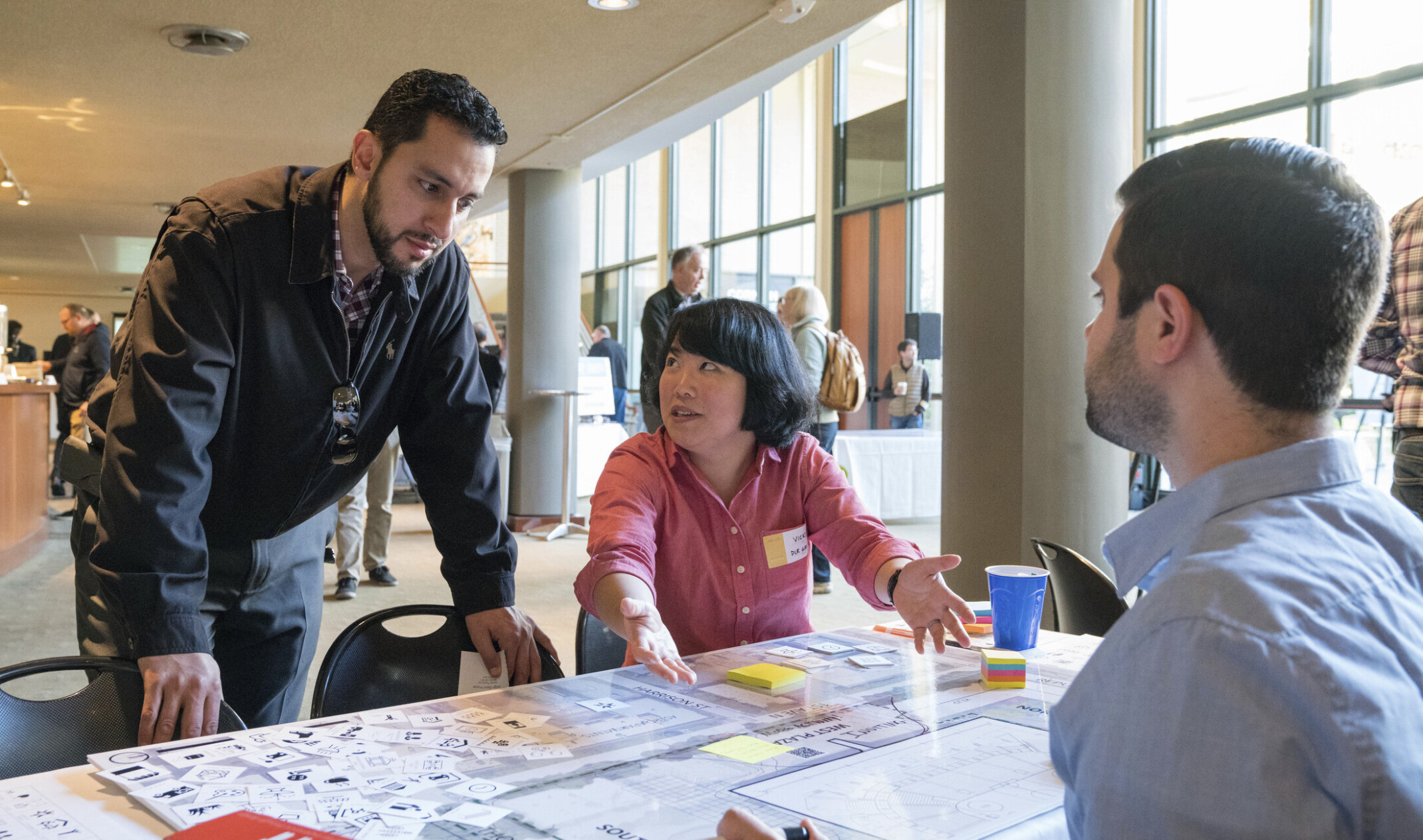 3 people in an animated discussion while ideating a design. A larger group stands behind.