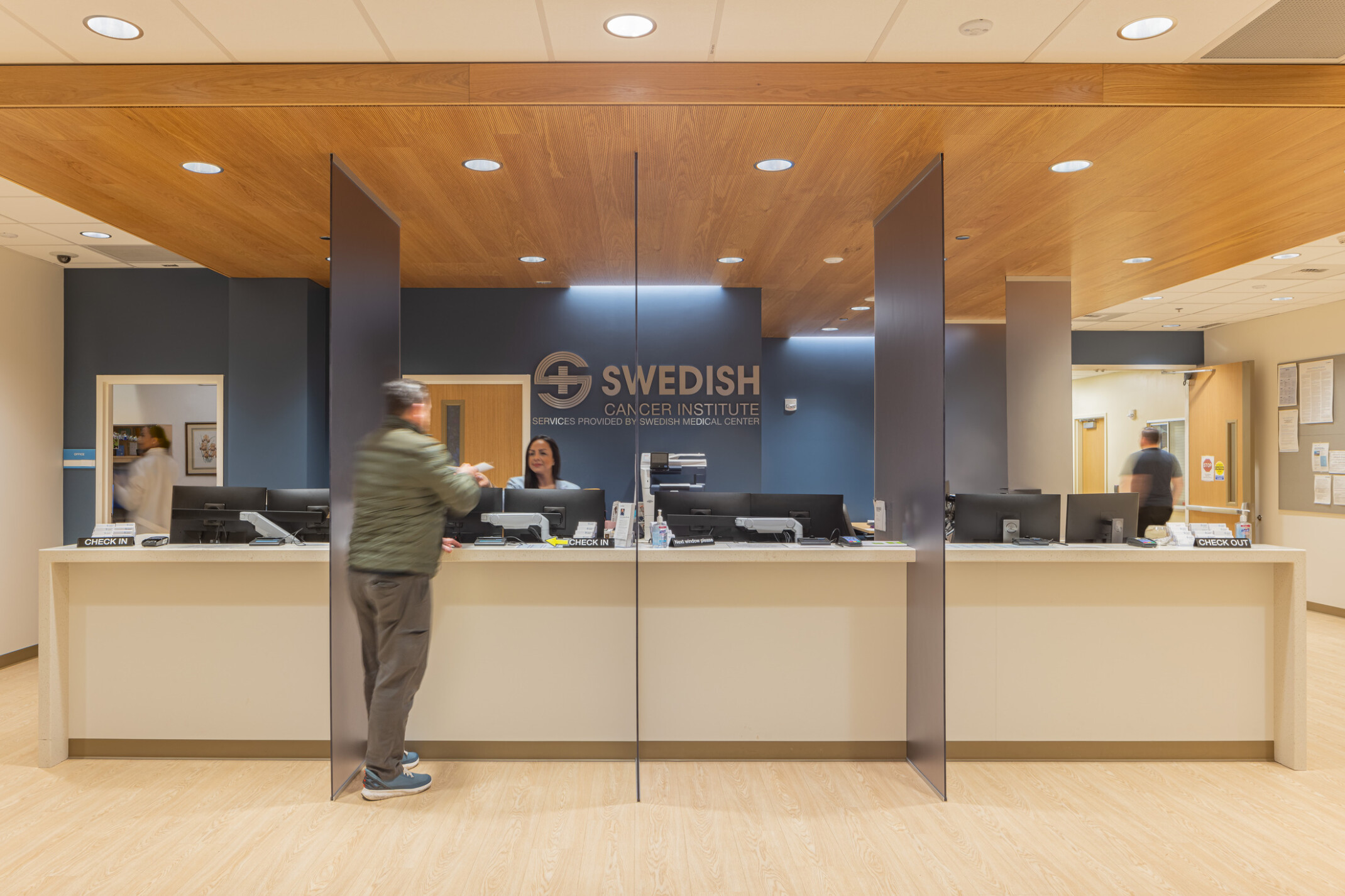 Light wood reception desk in front of a dark blue wall with silver letters that read Swedish Cancer Institute