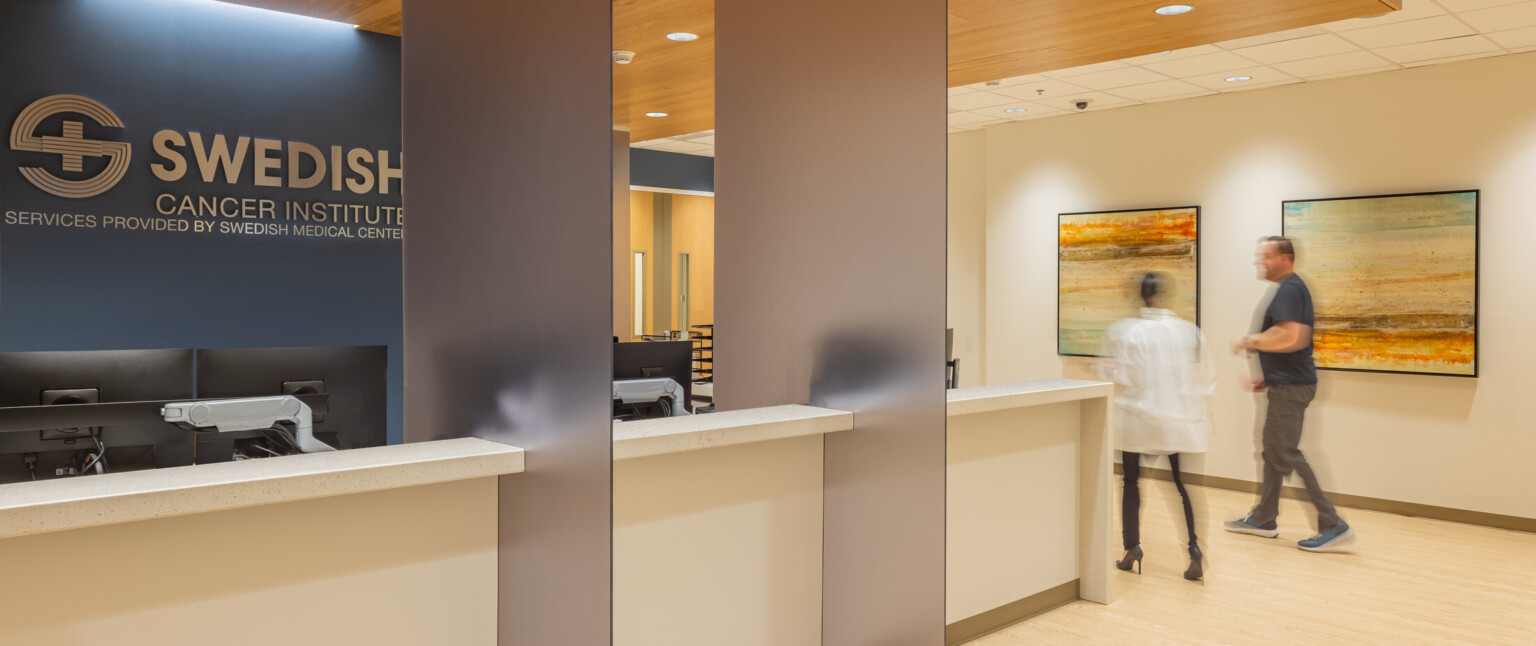 Light wood reception desk in front of a dark blue wall with silver letters that read Swedish Cancer Institute