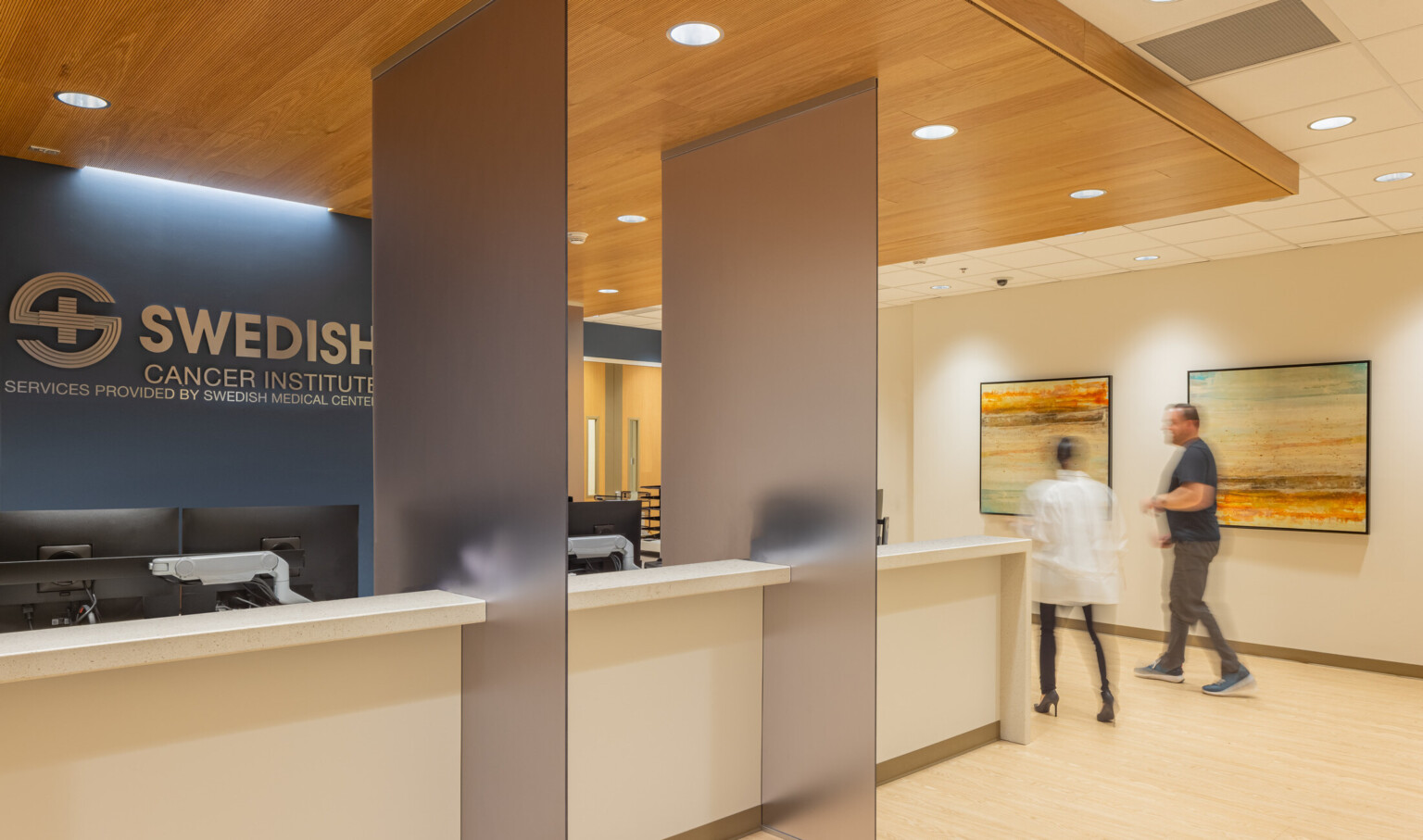Light wood reception desk in front of a dark blue wall with silver letters that read Swedish Cancer Institute
