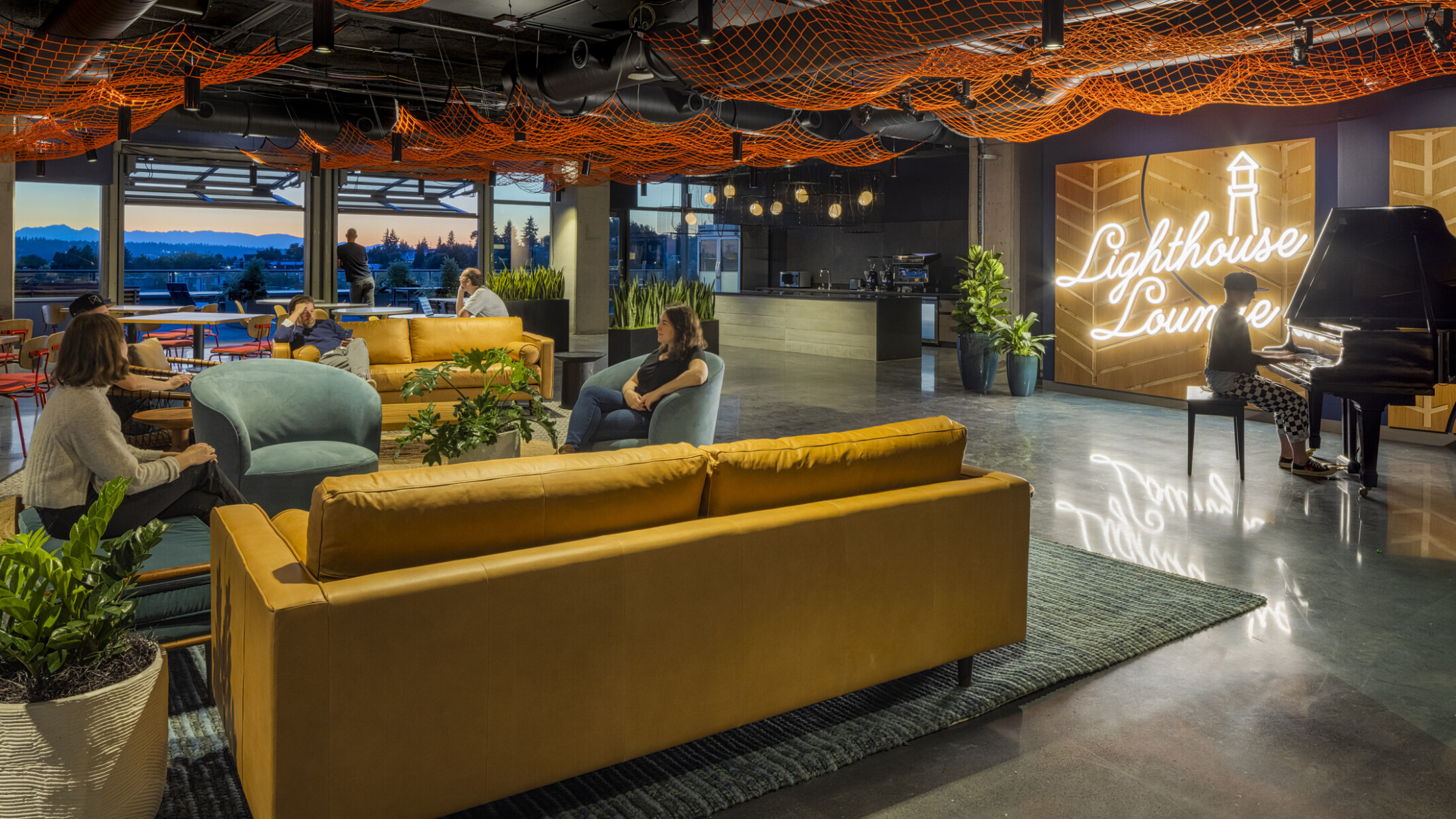 workplace lounge with piano and fishing net art installation, garage doors open to mountain views at sunset