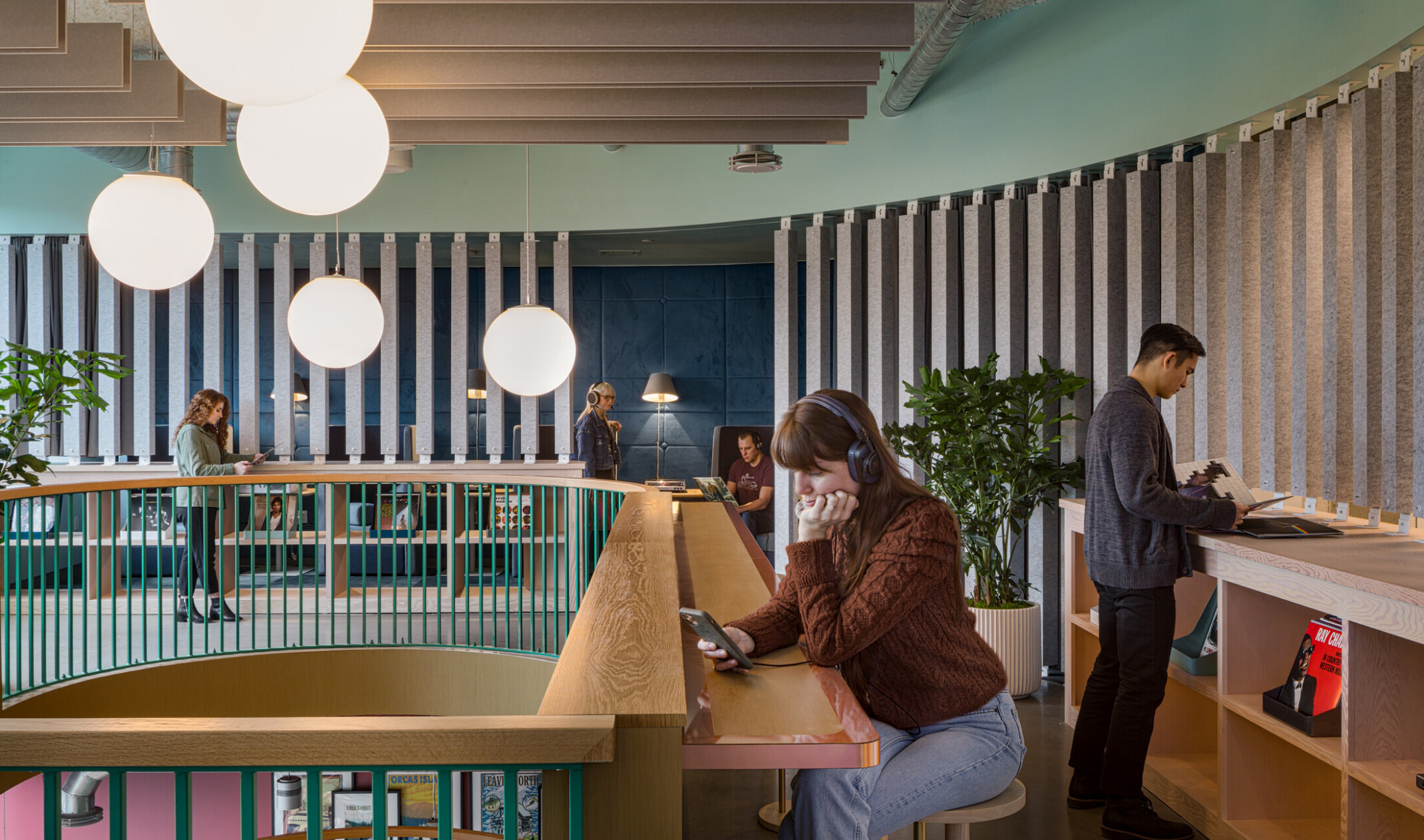 a woman on her phone with headphones sits at a radial wooden counter overlooking a mezzanine finished in wooden slats