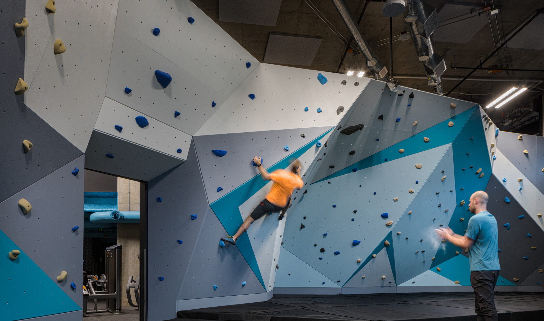 Rock wall in shades of blue with triangular patterns lining the walls. Exposed A/C ducting in the ceiling