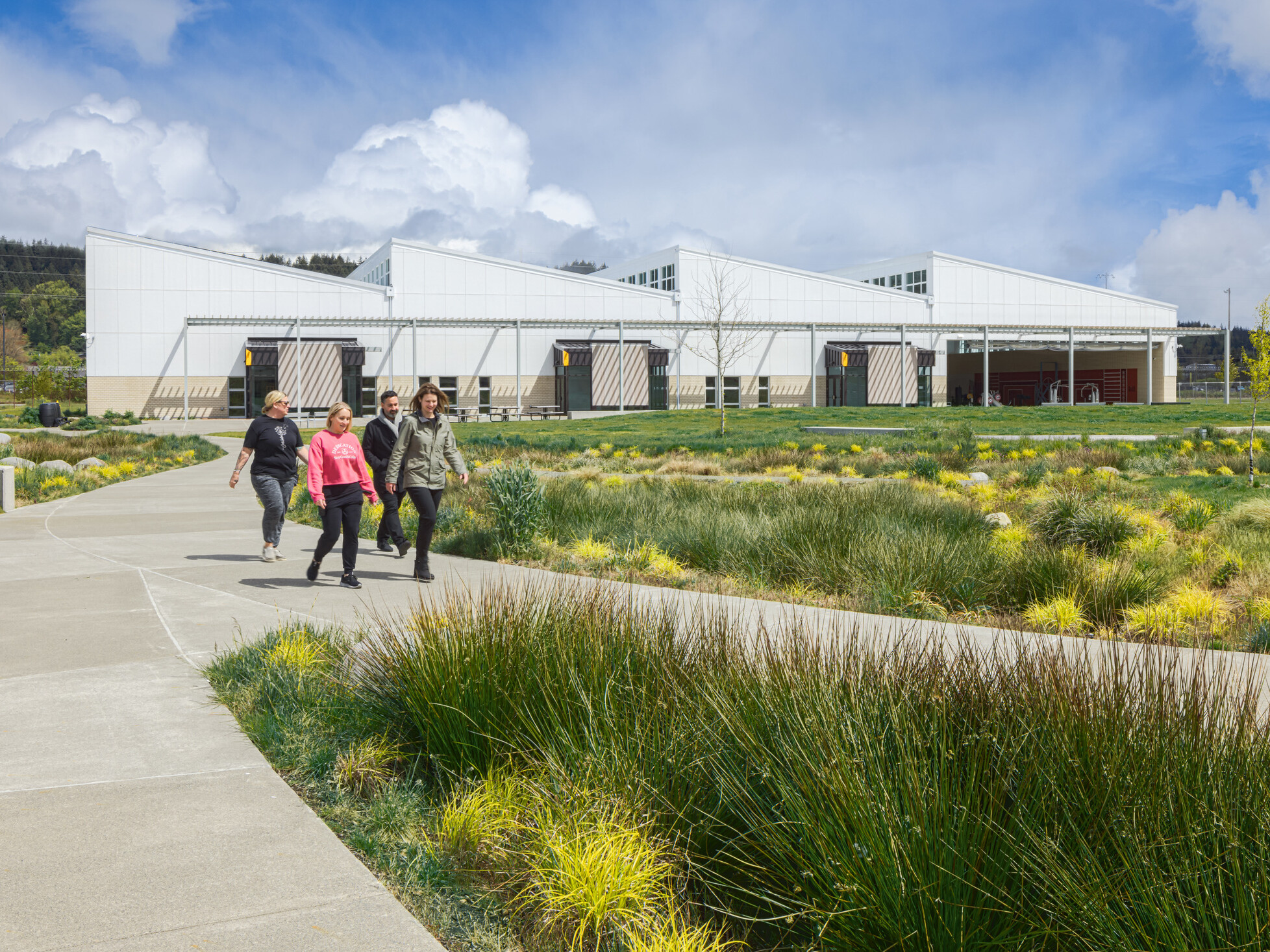 Exterior of the Green Hill school showing a modern white building with angled rooflines, with a covered awning spanning the building. Multiple concrete paths lined with lush landscaping