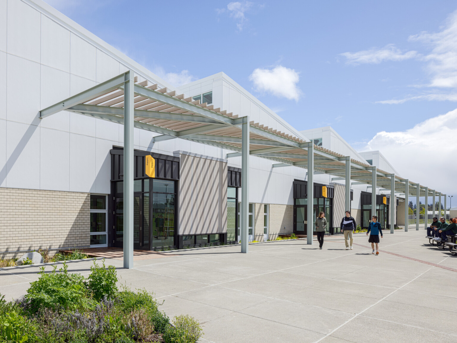 Modern building with angled rooflines with a sidewalk lined with a awning with multiple columns
