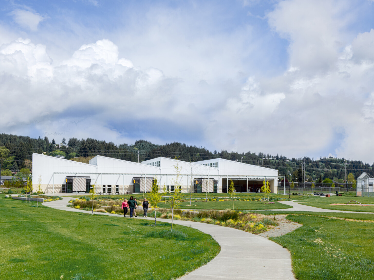 Looking down a sidewalk lined with lush green landscaping at a modern white building with angle rooflines.