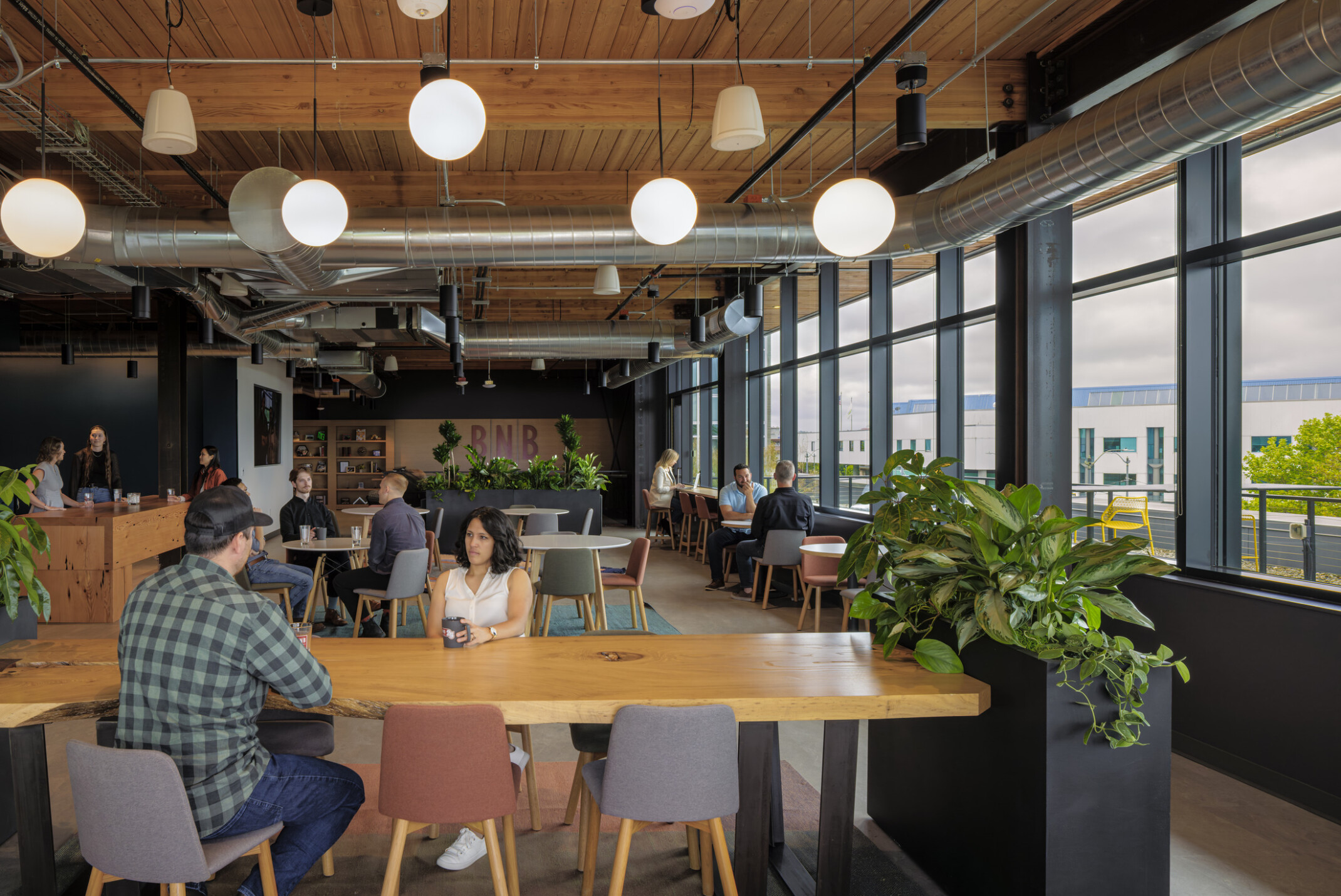 Employees gather in a work café with large windows with views outside; mixing casual conversations with heads-down work