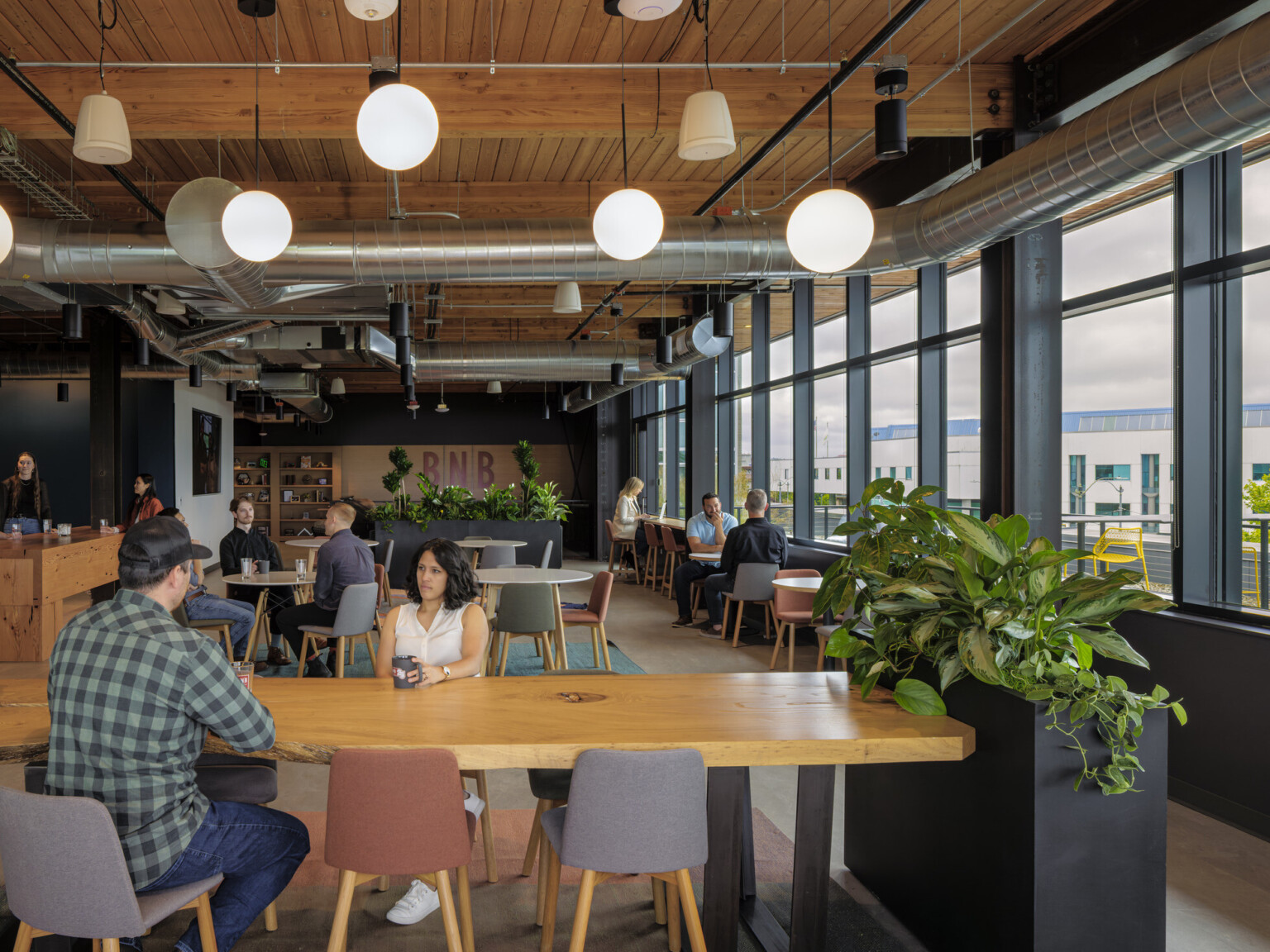 Employees gather in a work café with large windows with views outside; mixing casual conversations with heads-down work
