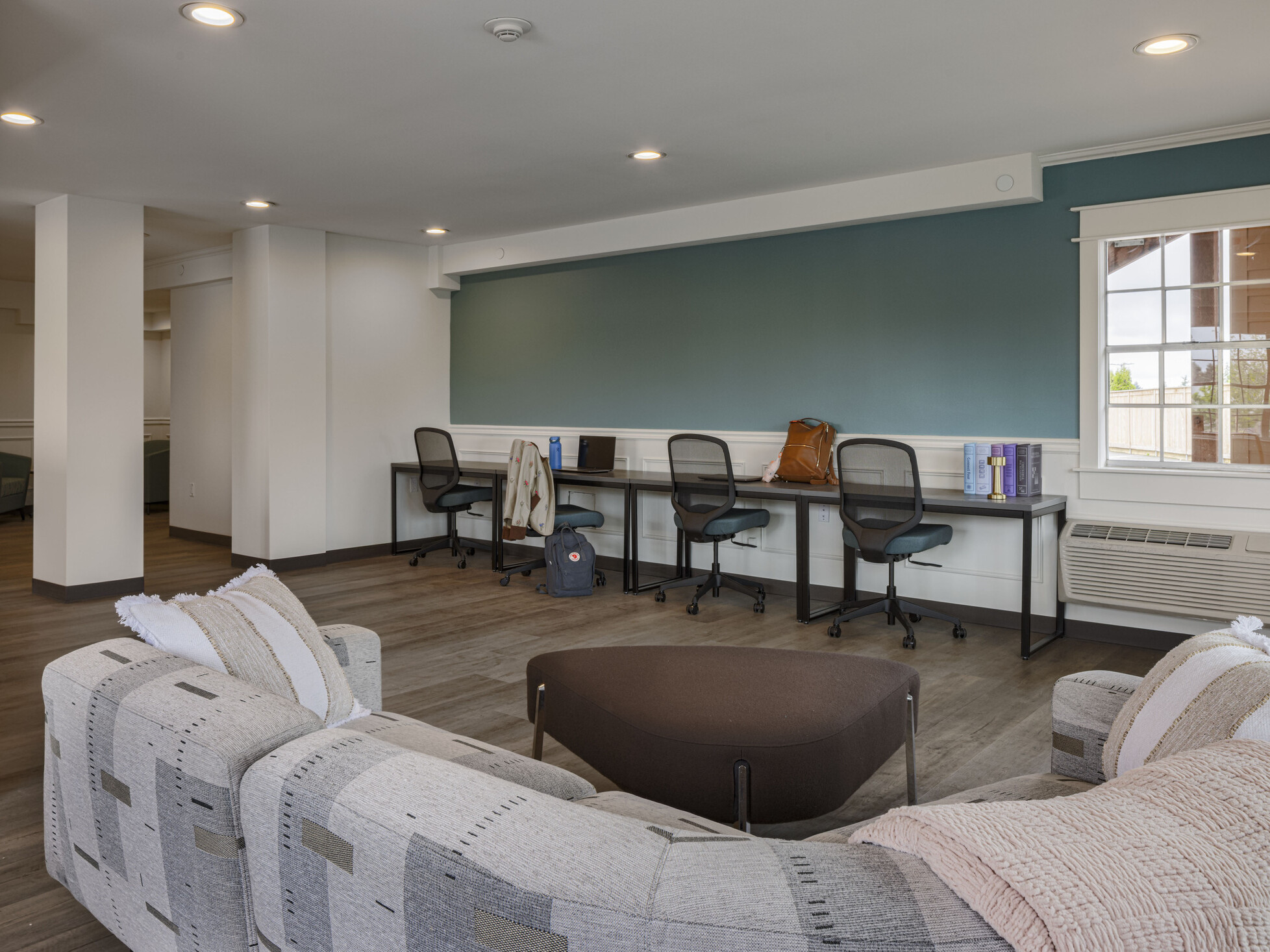 A community space includes a sofa, multi-seat desk area, bright lighting, and green accent walls.