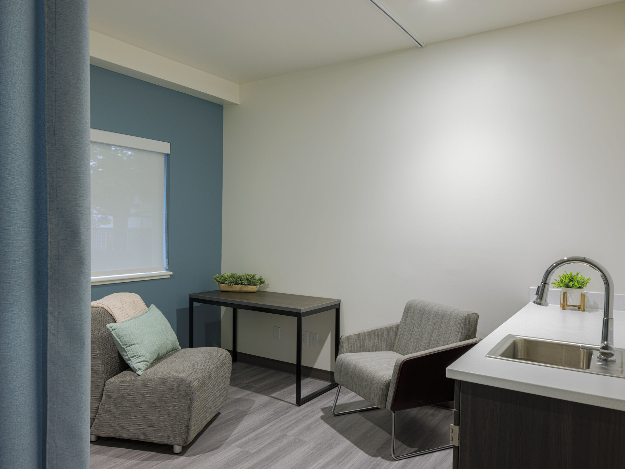 A private corner includes a curtain, blue accent wall with window, comfortable seating, and a counter with a sink and faucet.