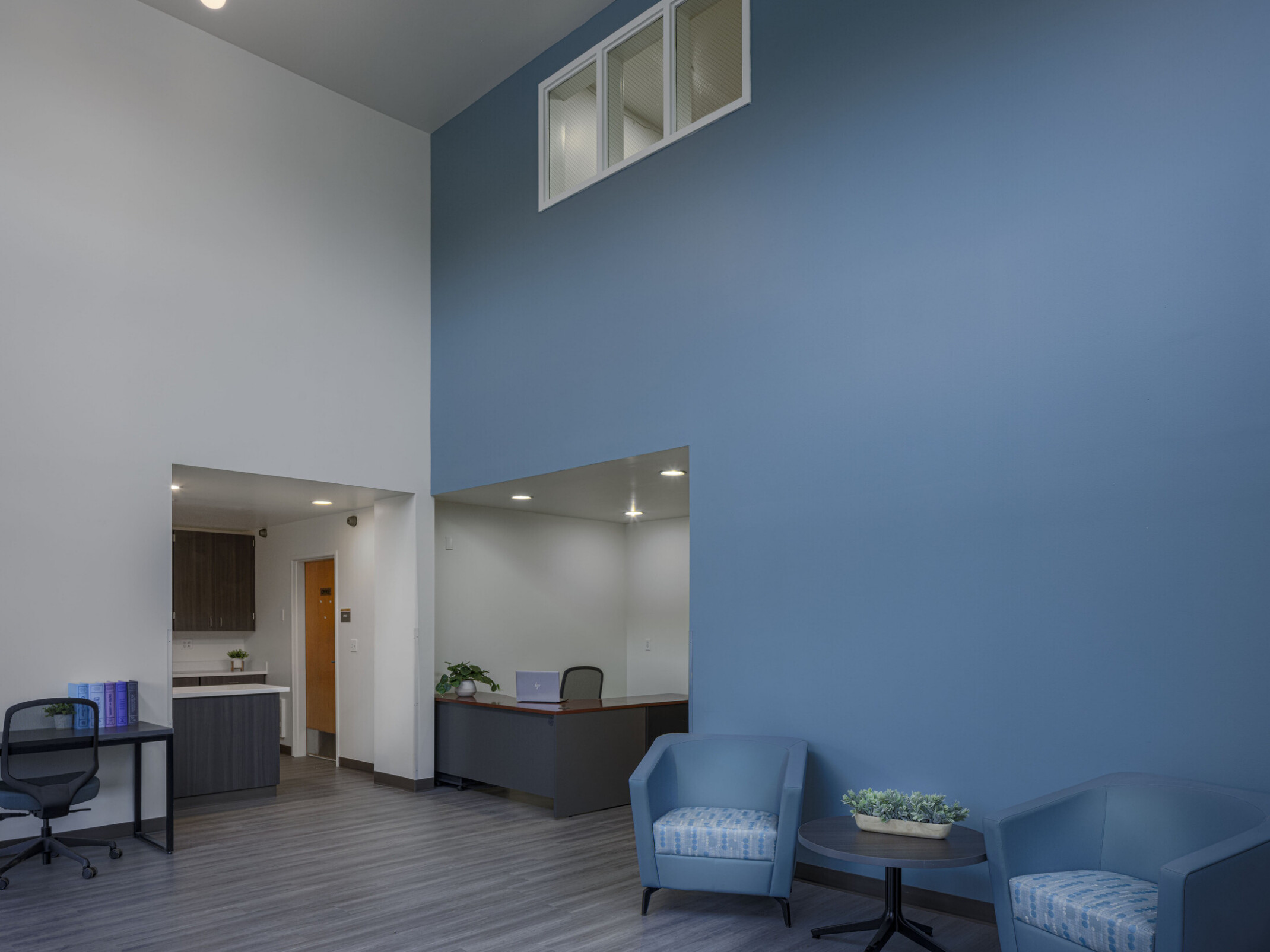 A central lobby-like area is shown with a prominent blue wall, matching lounge chairs, a receiving desk at the rear, and a kitchenette to the left