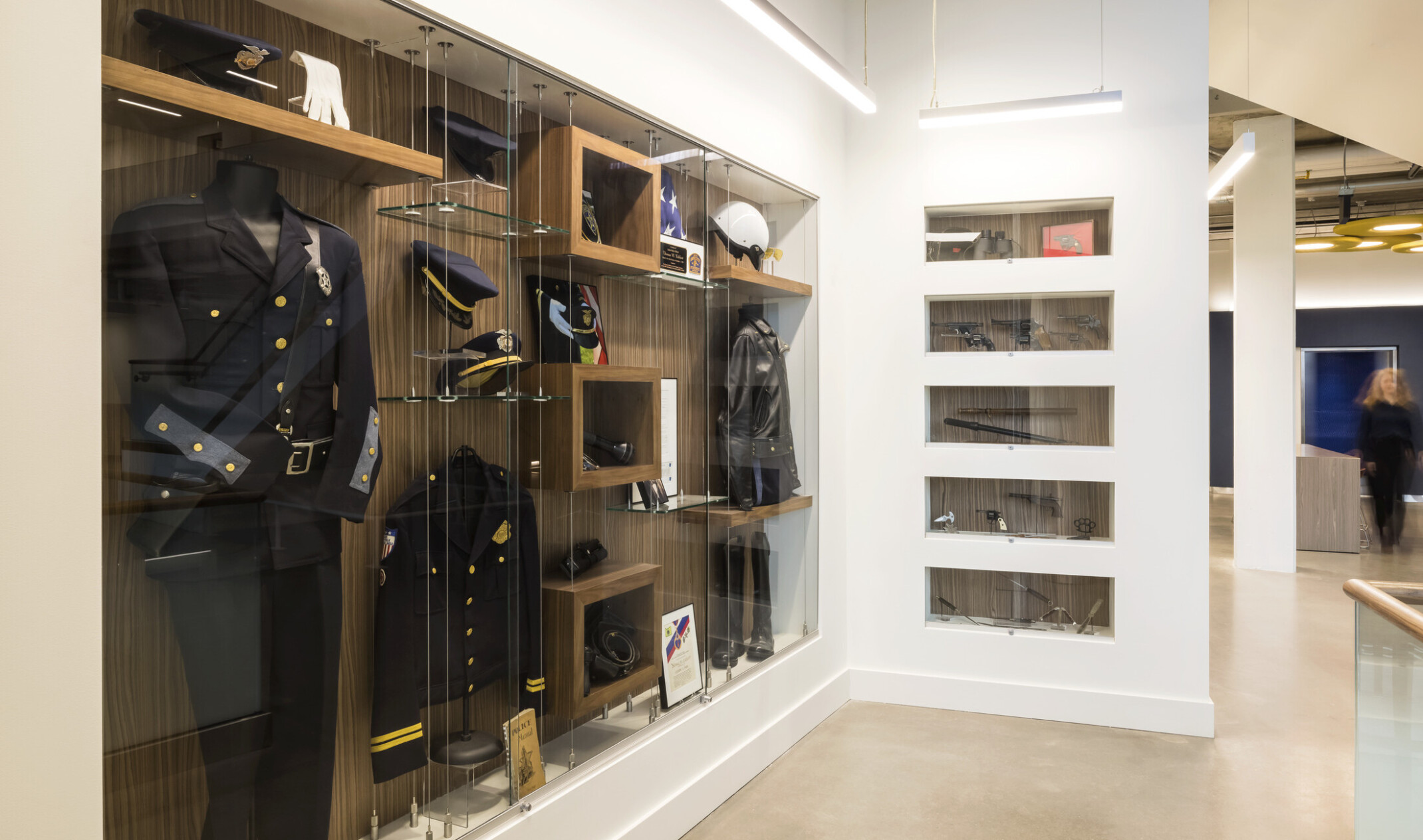 Display case behind glass in white wall. Police uniform and awards.