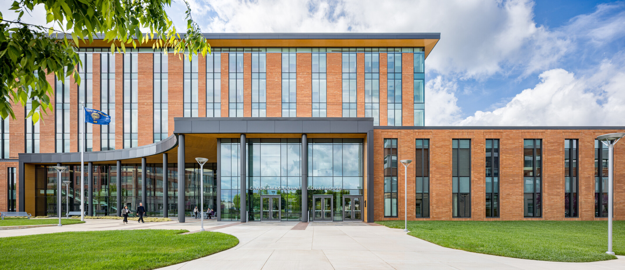 Front of a modern courthouse building featuring a mix of tan brick and expansive glass panels. Glass entrance is framed by a dark, horizontal overhang and vertical columns