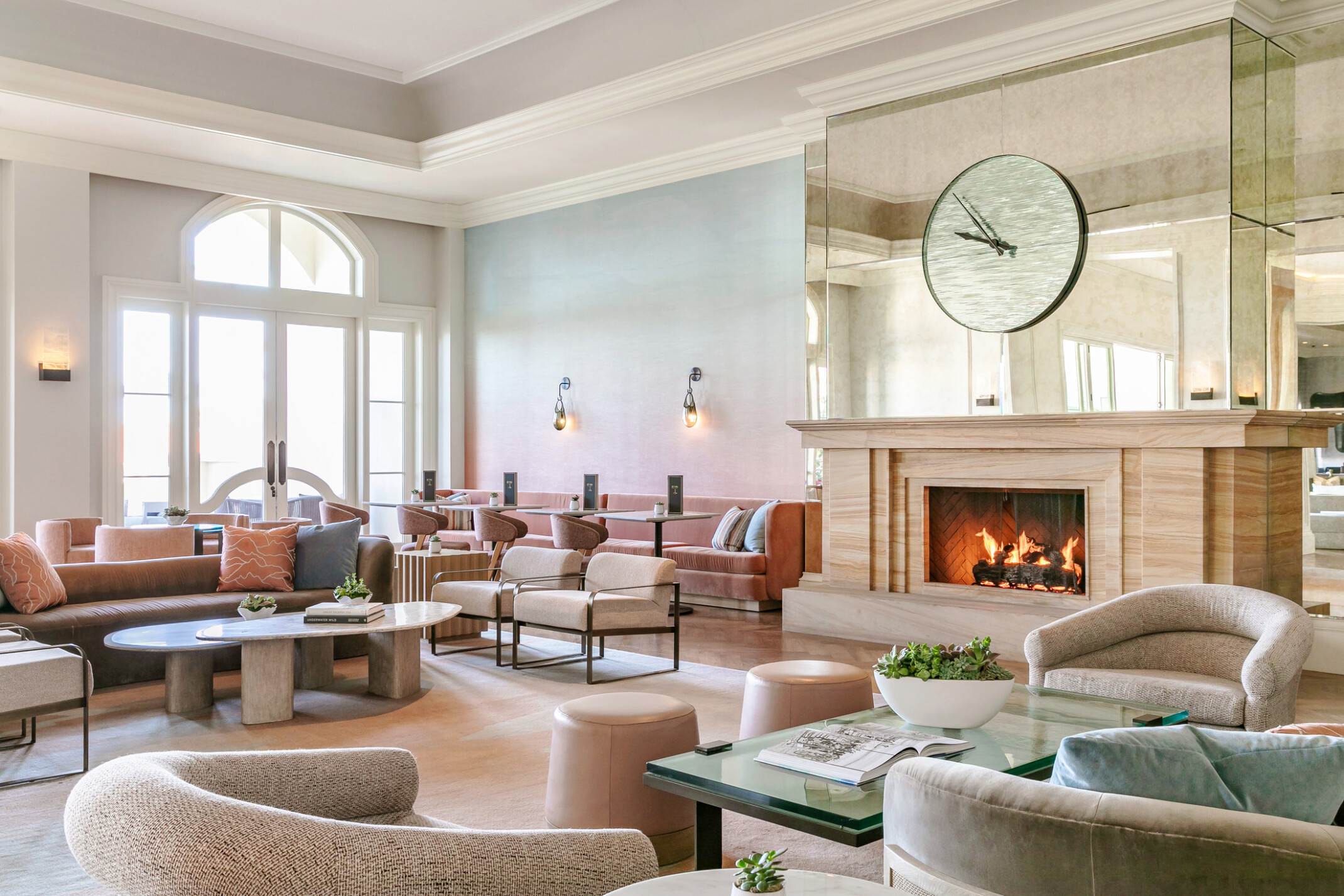modern and airy beach resort lobby with muted tones, fireplace, large clock on a mirrored wall, and scones lighting the space