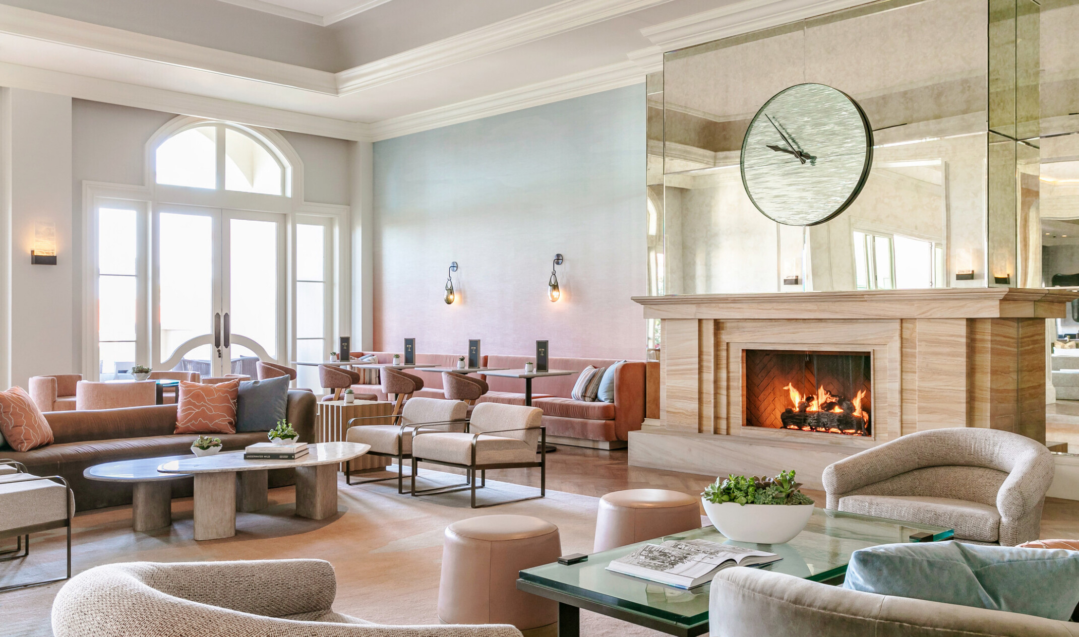 modern and airy beach resort lobby with muted tones, fireplace, large clock on a mirrored wall, and scones lighting the space