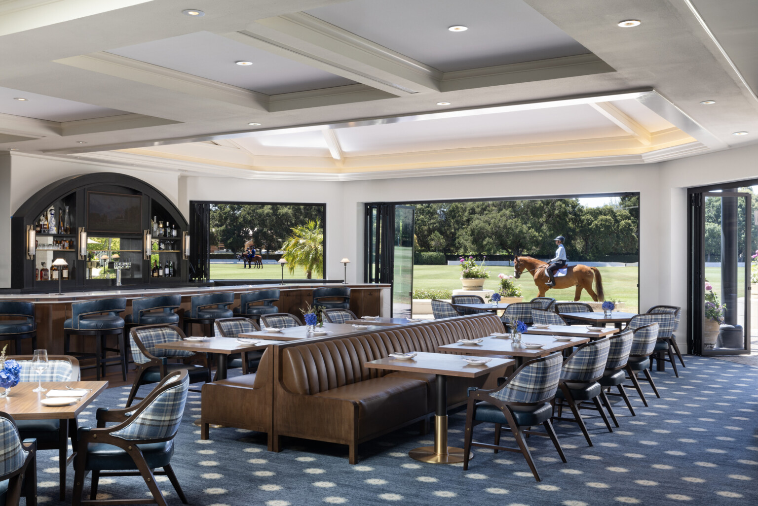 view from inside the dining room at a luxury country club, equestrian rider in background, blue carpet and wood details fill the space