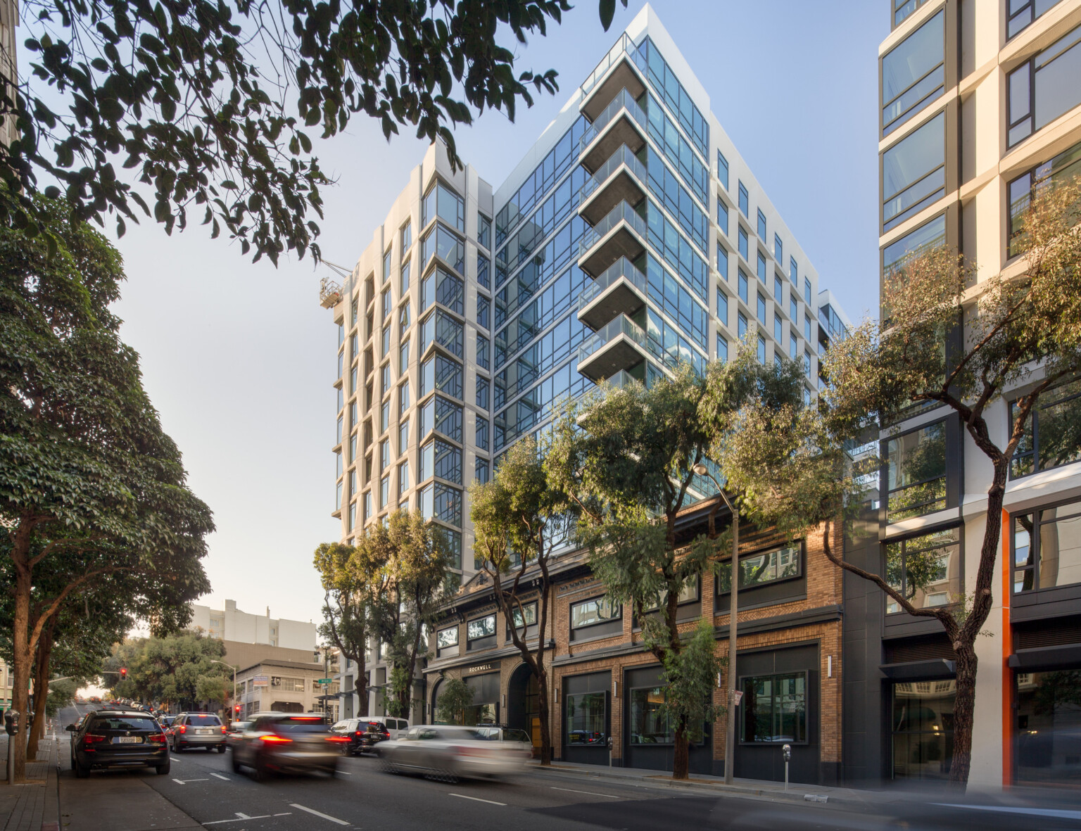 High-rise building with glass facade and balconies along a tree-lined street.