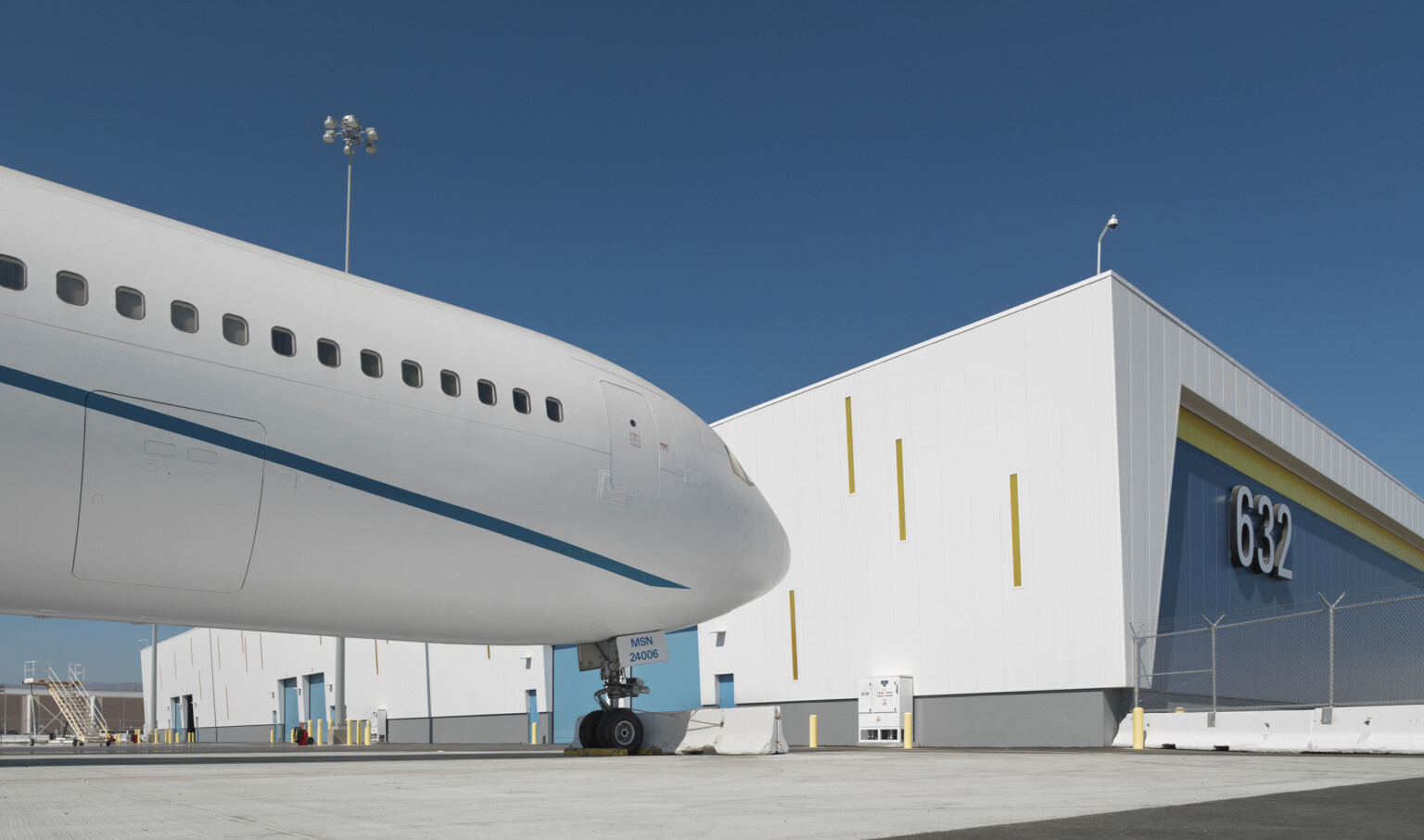 Corner view of blue and yellow building with white wrapped facade with yellow accents on side facing plane with loading doors