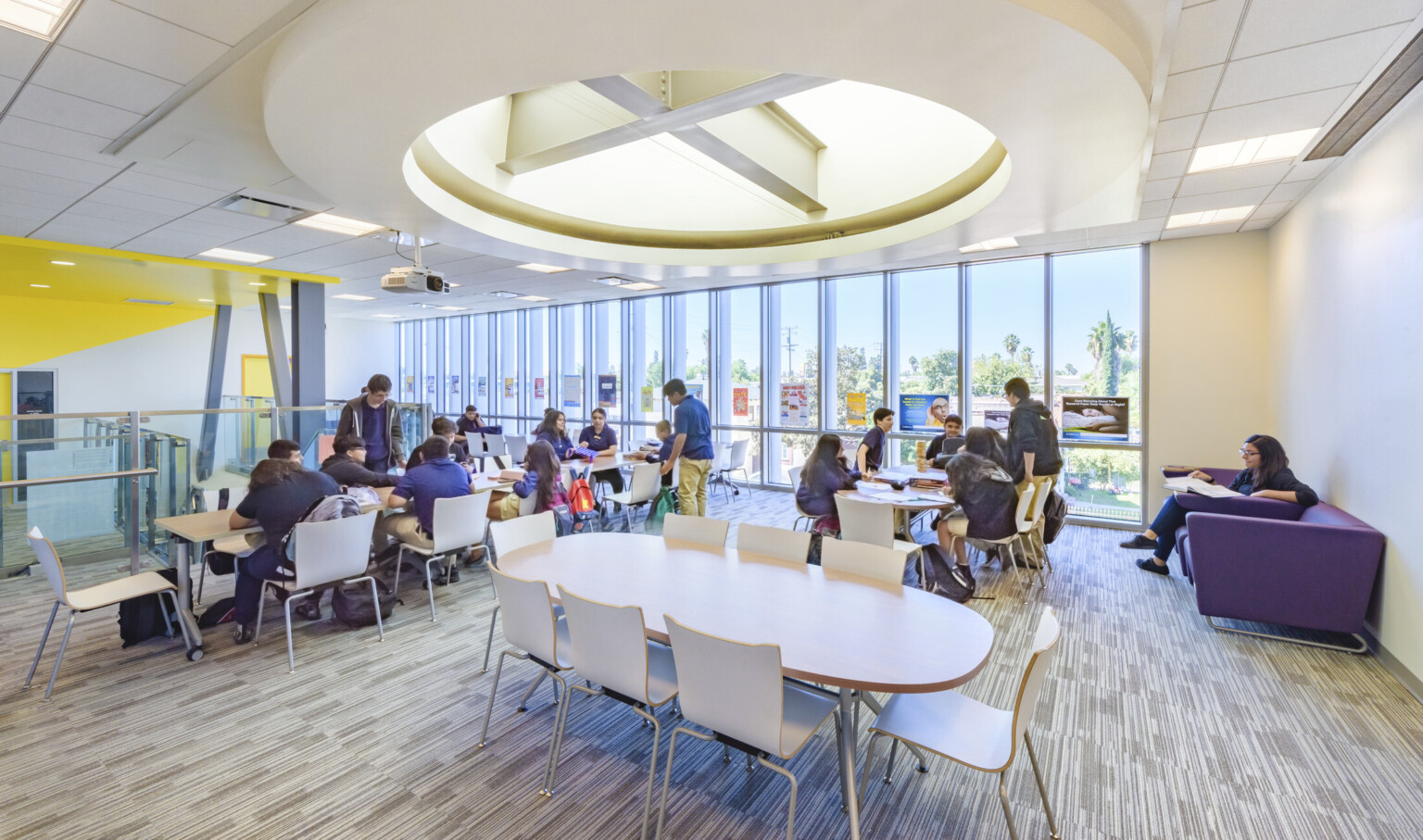 Floor to ceiling windows in white room with tables and chairs. Round recessed ceiling detail with exposed beams and lighting