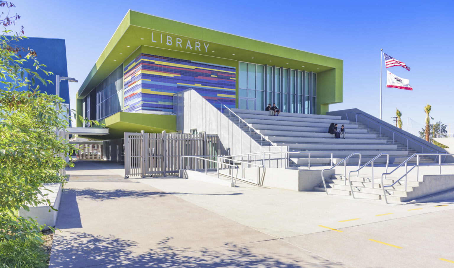 Corner view of lime library, multicolor tile wraps around left side between floor to ceiling windows. Grey steps in front