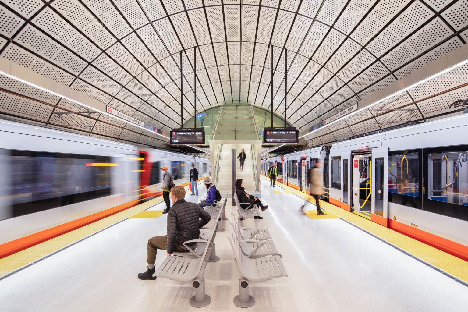 Rounded tunnel covered in perforated white panels. Hanging light beams along tracks beside screens