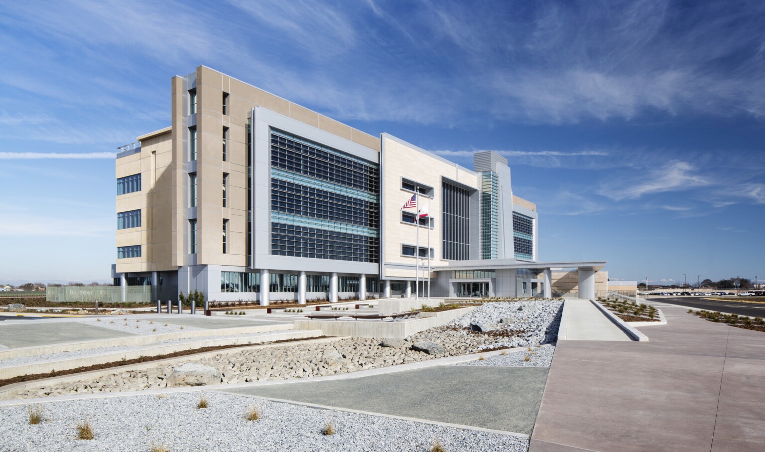 Side view of building exterior from base of ramp. Rock gardens line the ramp path. Beige facade at sides of building