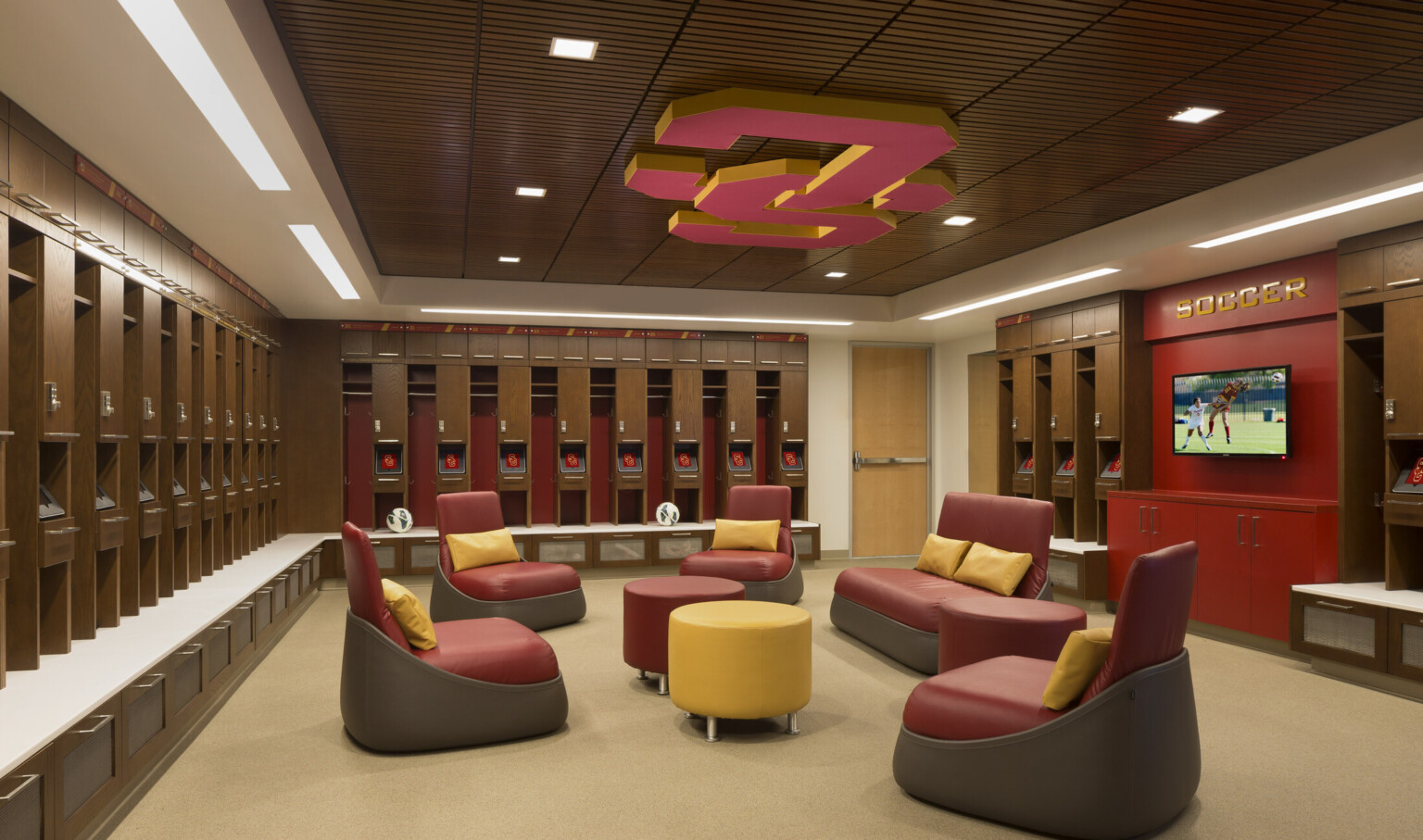 Wood lockers with seating bench line room with recessed wood panel ceiling and red SC logo. Seating area by red accent wall