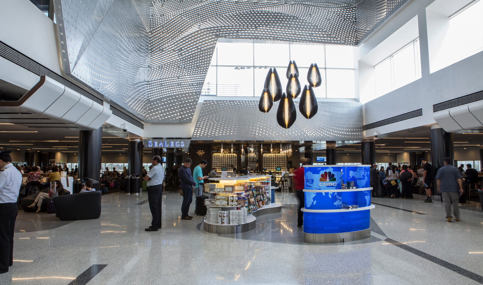Pendant lights above kiosk in double height room. Large windows (front, right), silver perforated panel accents (front, left)