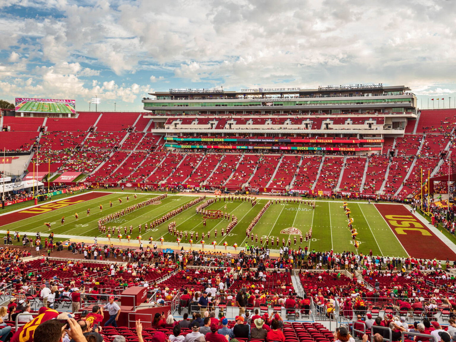 Students form letters USC on football field surrounded by red bleachers. Box seating opposite. Red end zones with yellow USC