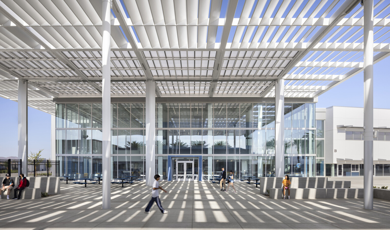 Under white paneled shade canopy supported by white columns looking to triple height glass facade entry
