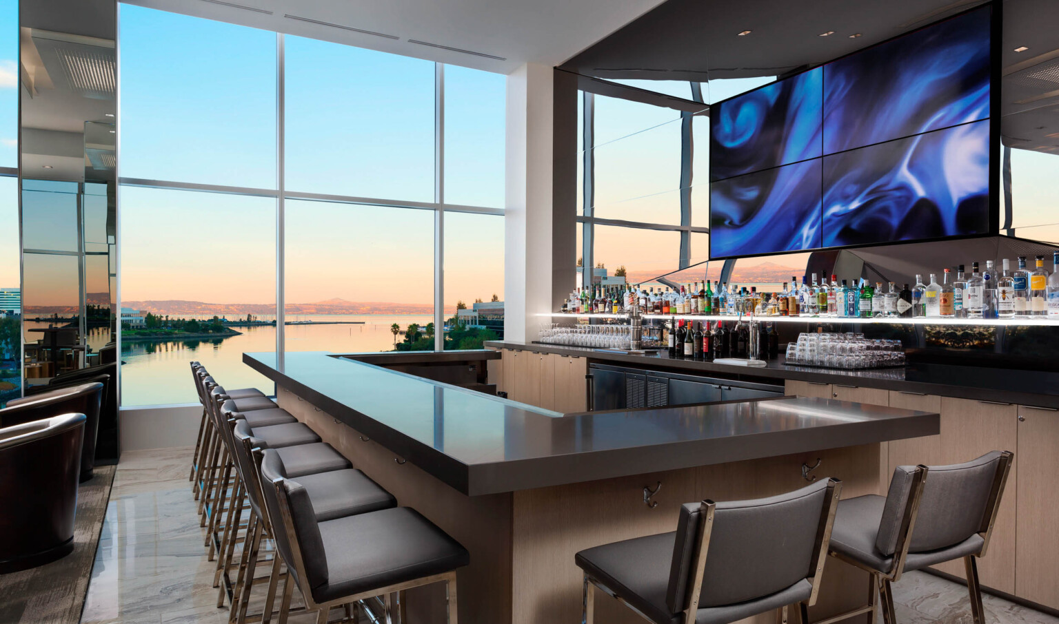 Wood bar with grey counter in room with floor to ceiling windows in front of mirror with central abstract swirling panels